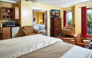 A hotel room with a bed, a dresser, a chair, a TV, and a view of the outdoors.