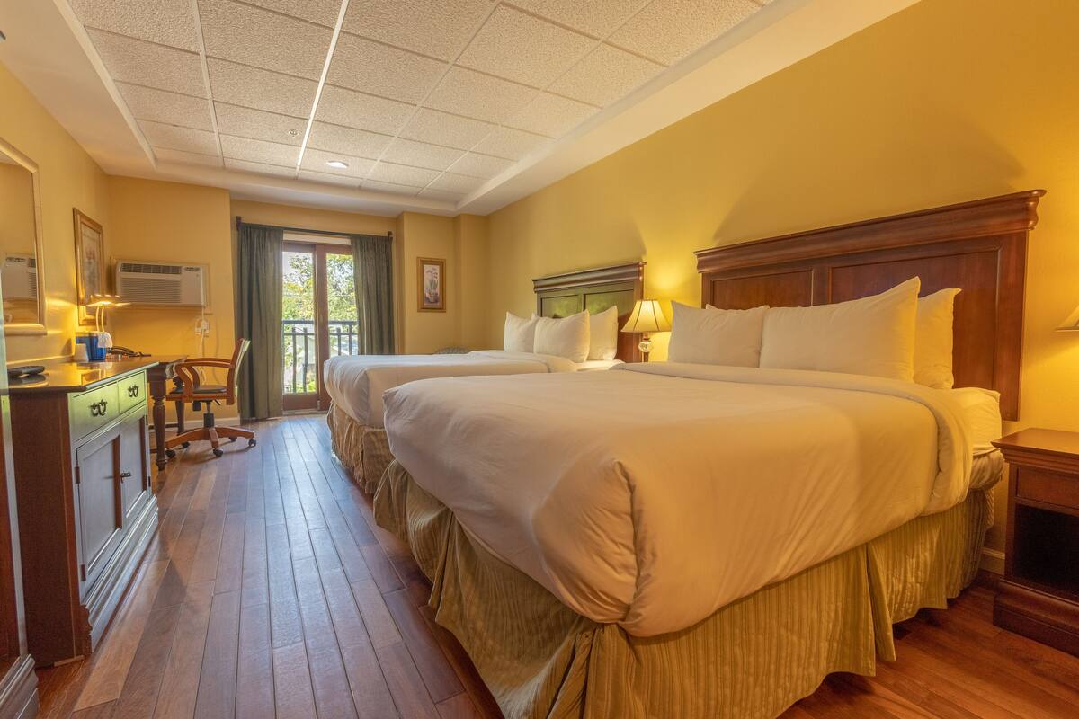A hotel room with two large beds, a desk with a chair, a dresser, and a window with a view of the outdoors.