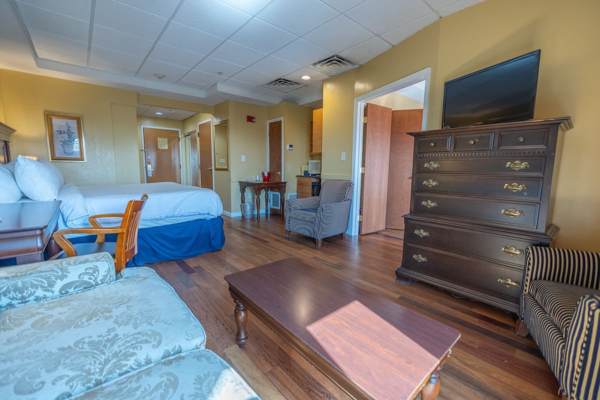 A hotel room with a bed, a wooden dresser, a television, a chair, and a sofa.
