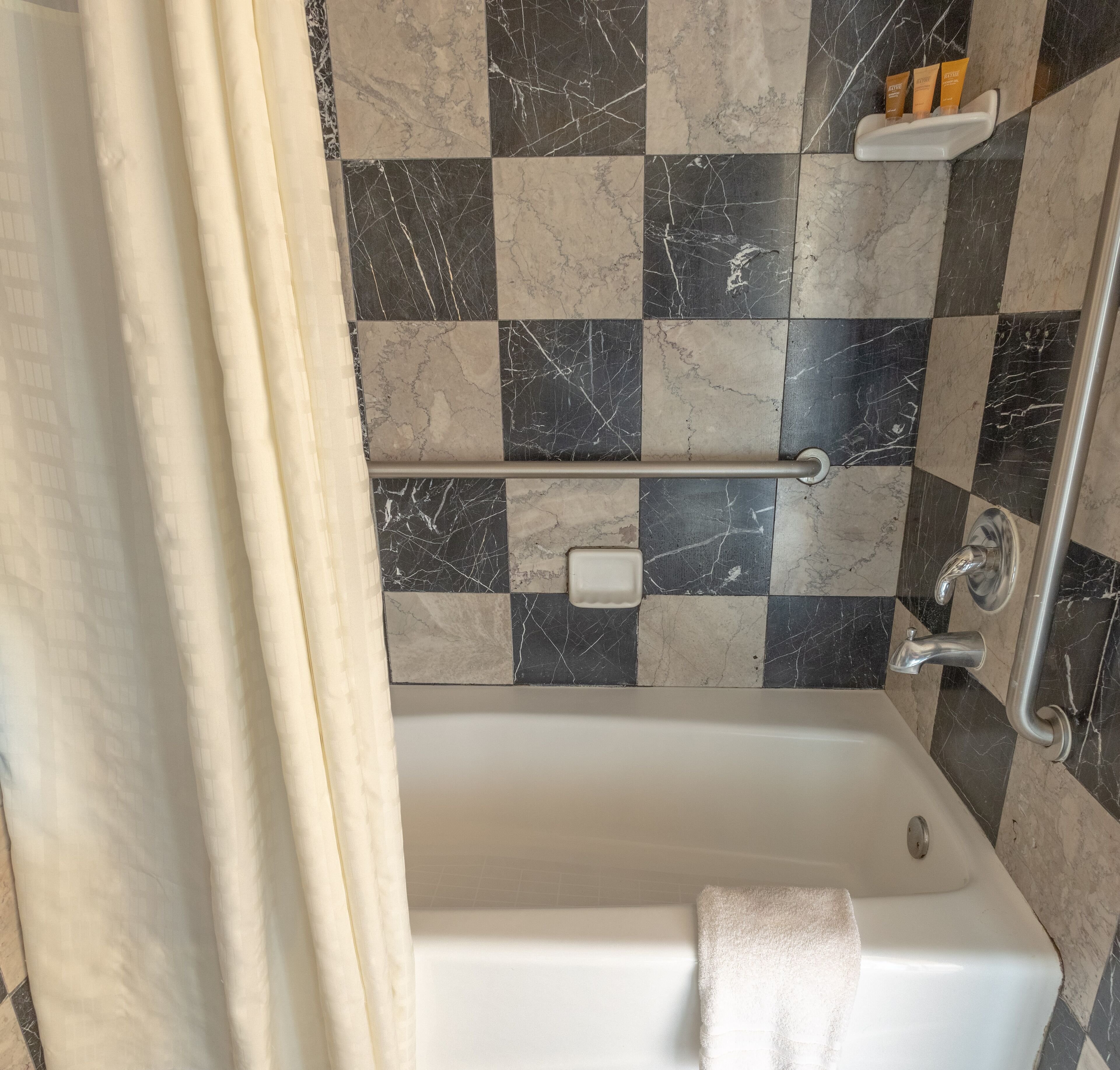 Une salle de bain avec un mur recouvert de carreaux à motifs, une baignoire, une serviette et une étagère contenant des articles de toilette.