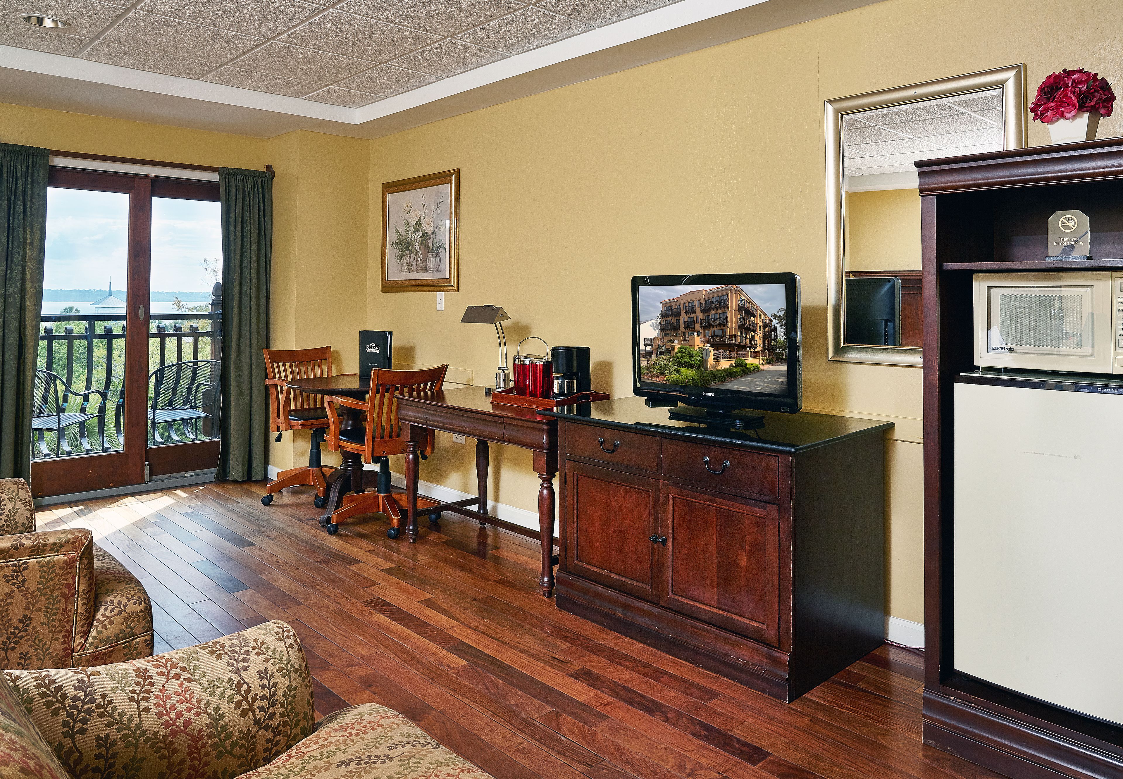 Habitación de hotel con escritorio de madera, televisor, refrigerador y balcón con vistas.