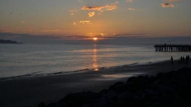 A sunset over a calm sea with a pier extending into the water.