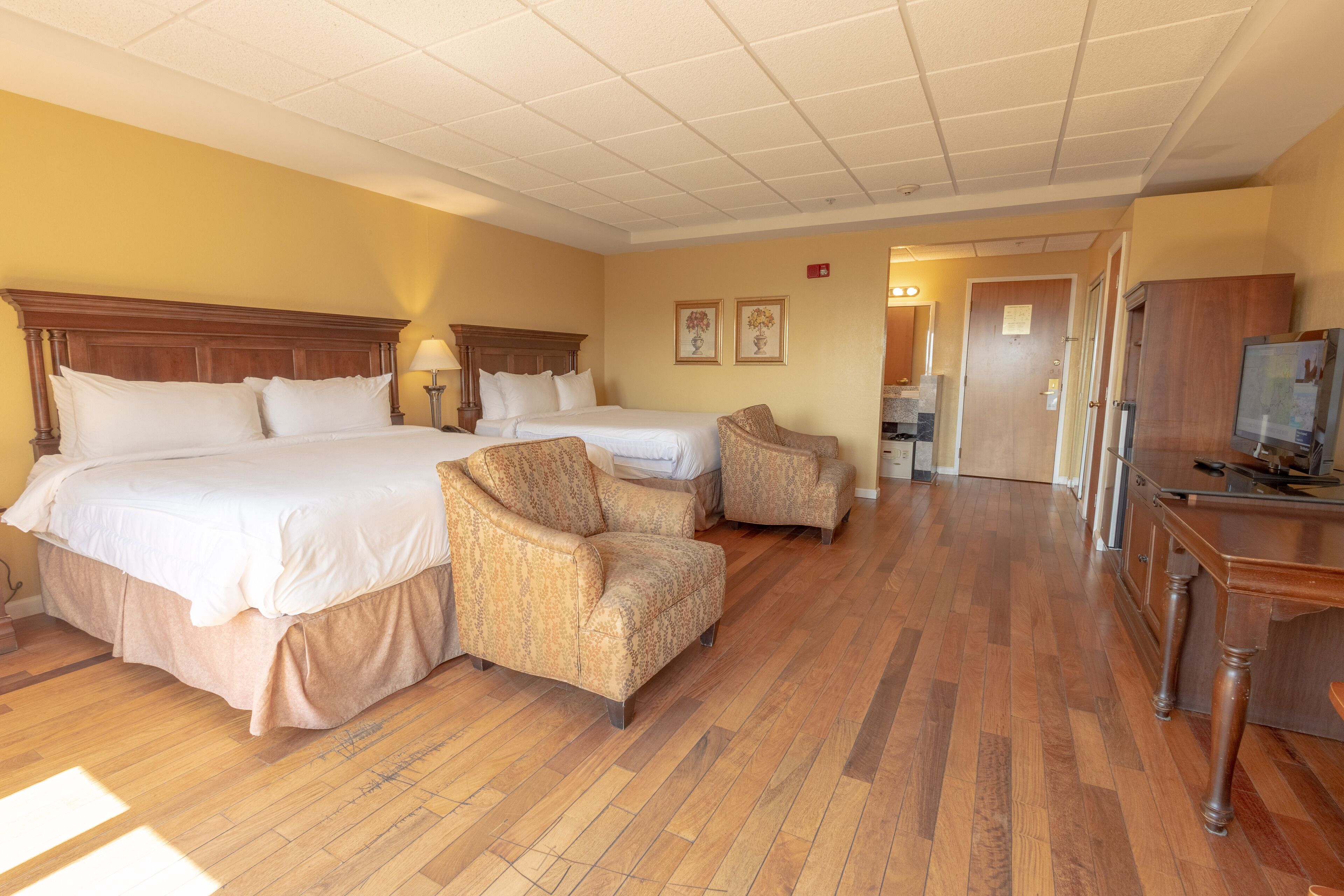 Habitación de hotel con dos camas, zona de estar con sillas, suelo de madera y televisor.