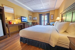 A hotel room with a large bed, a desk with a computer, a television, and a window with curtains.
