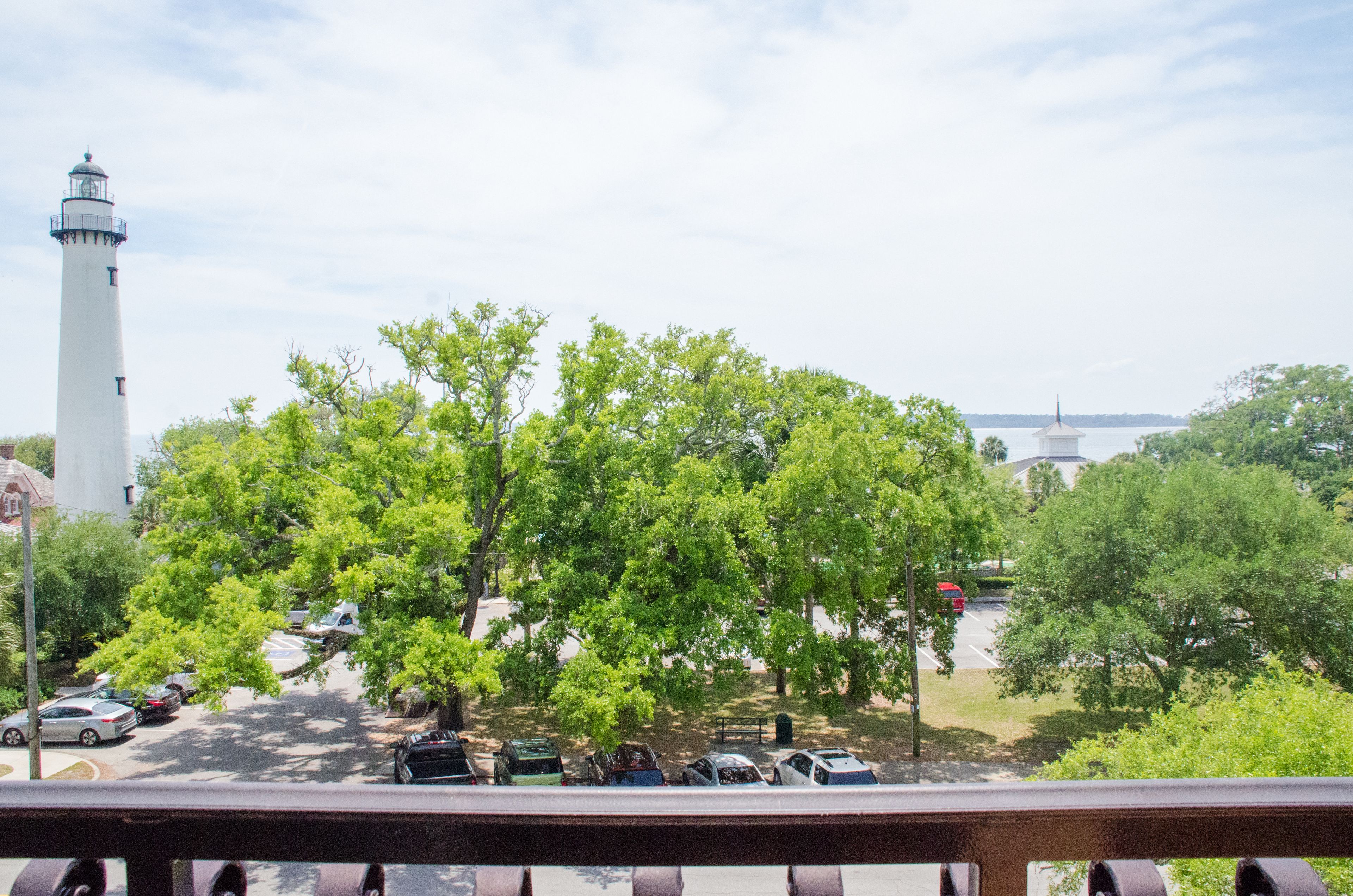 A view of a lighthouse, trees, and parked cars from a balcony.