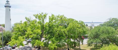 A view of a lighthouse, trees, and parked cars from a balcony.