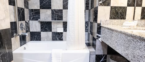 Un baño con piso de mármol blanco y negro a cuadros, una bañera blanca y un lavamanos con encimera de mármol.