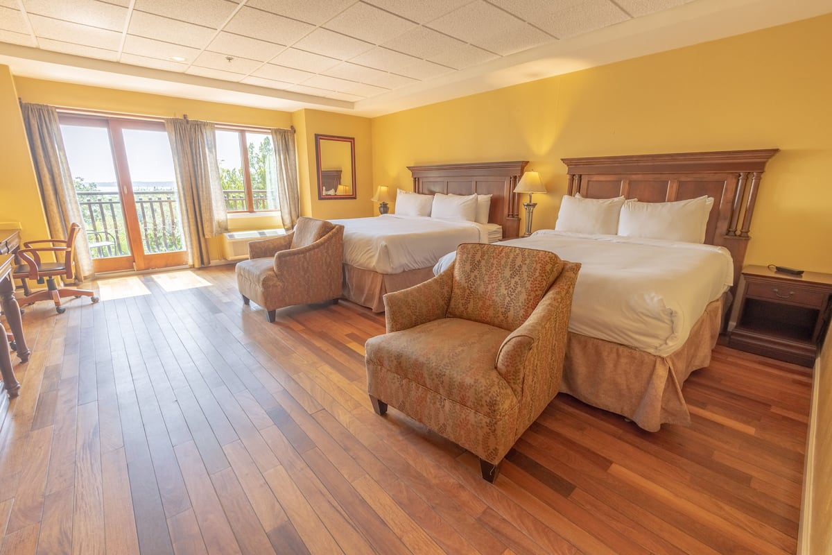 A hotel room with two beds, a chair, a desk, and a balcony with curtains.