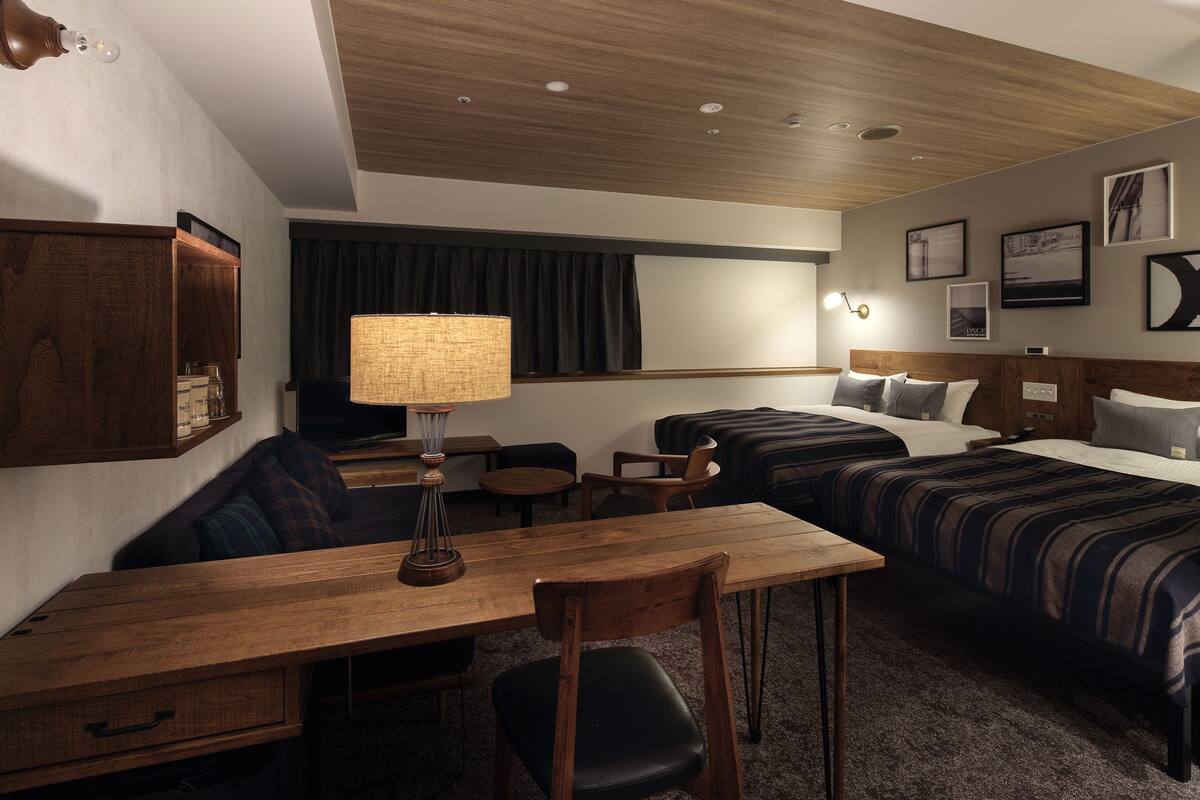 Una habitación de hotel con un escritorio de madera, dos camas, un sofá y una lámpara.