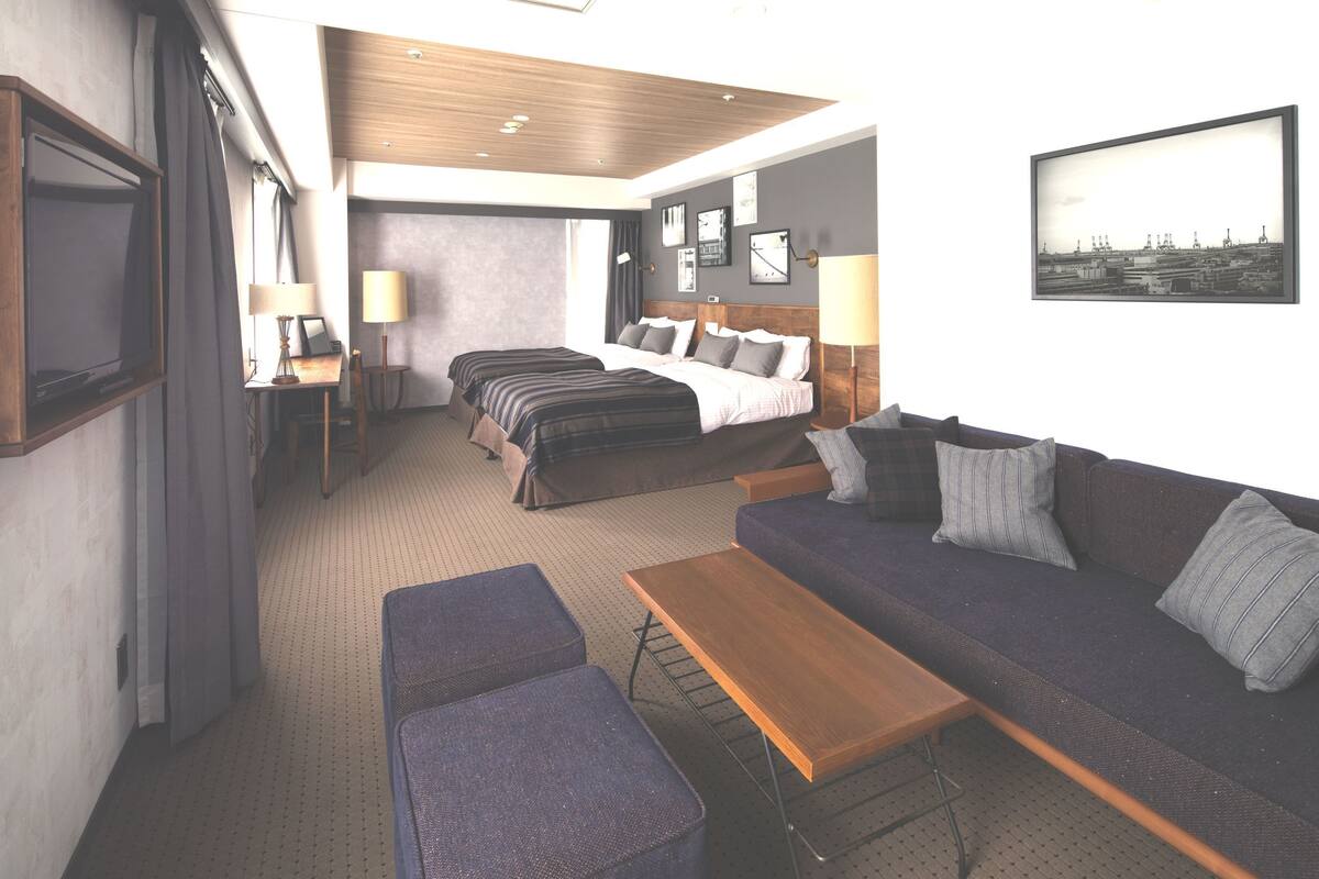 Habitación de hotel con una cama grande, un sofá, una mesita y un escritorio. Hay dos lámparas a cada lado de la cama y un cuadro en la pared.
