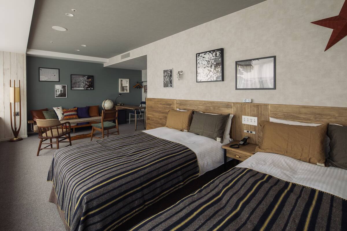Habitación de hotel con dos camas, un escritorio, una silla y un ventanal grande.
