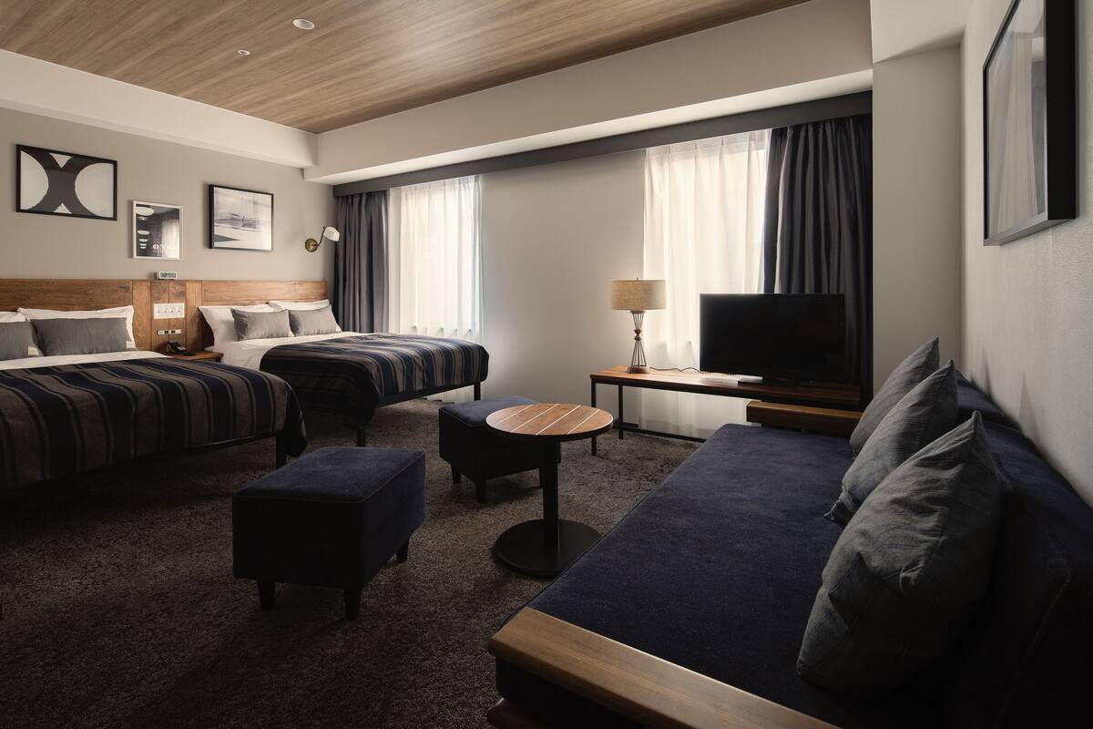 Habitación de hotel con dos camas, un sofá, un televisor y una mesita.