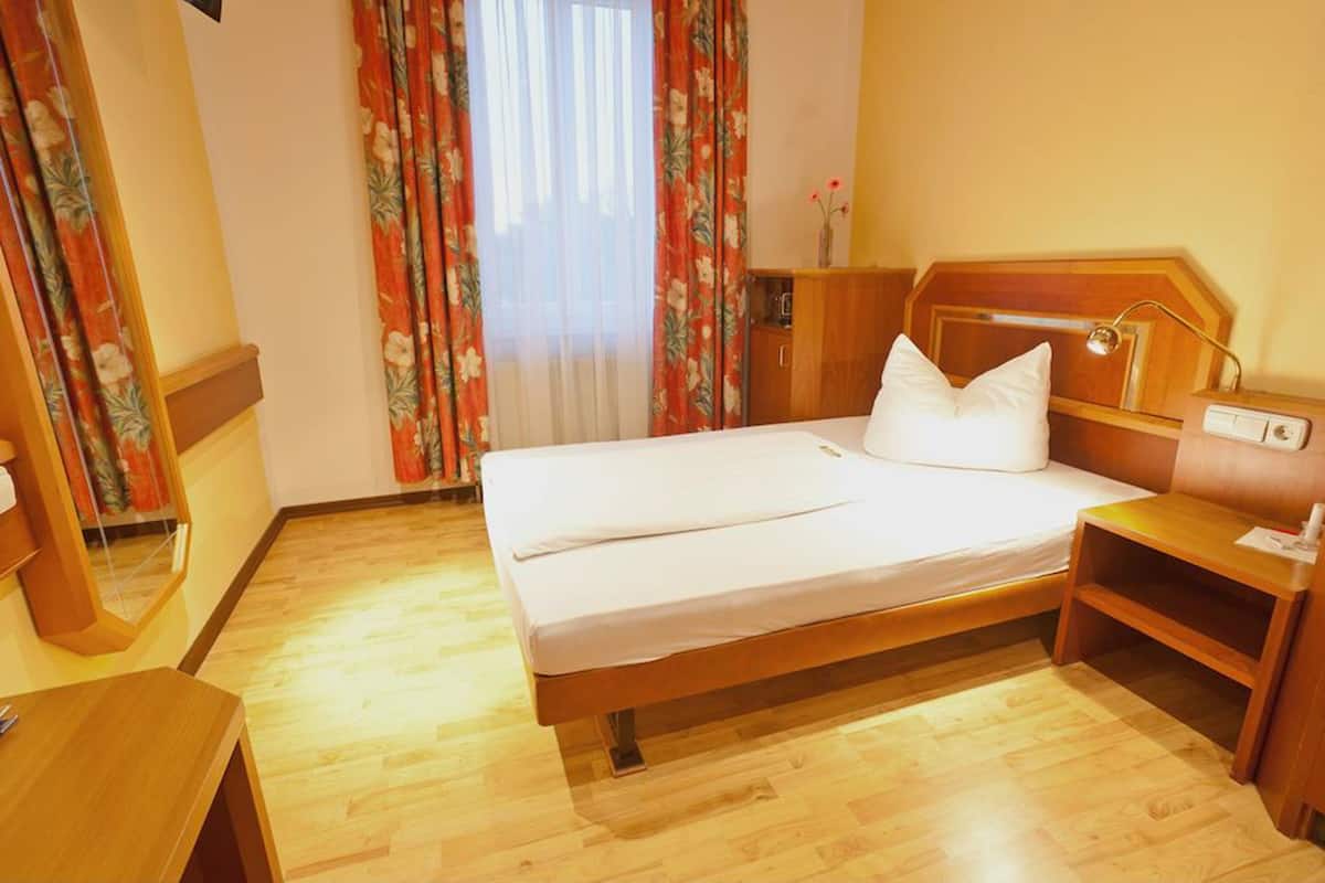 A hotel room with a wooden bed, a bedside table, a nightstand, a mirror, and a window with floral curtains.