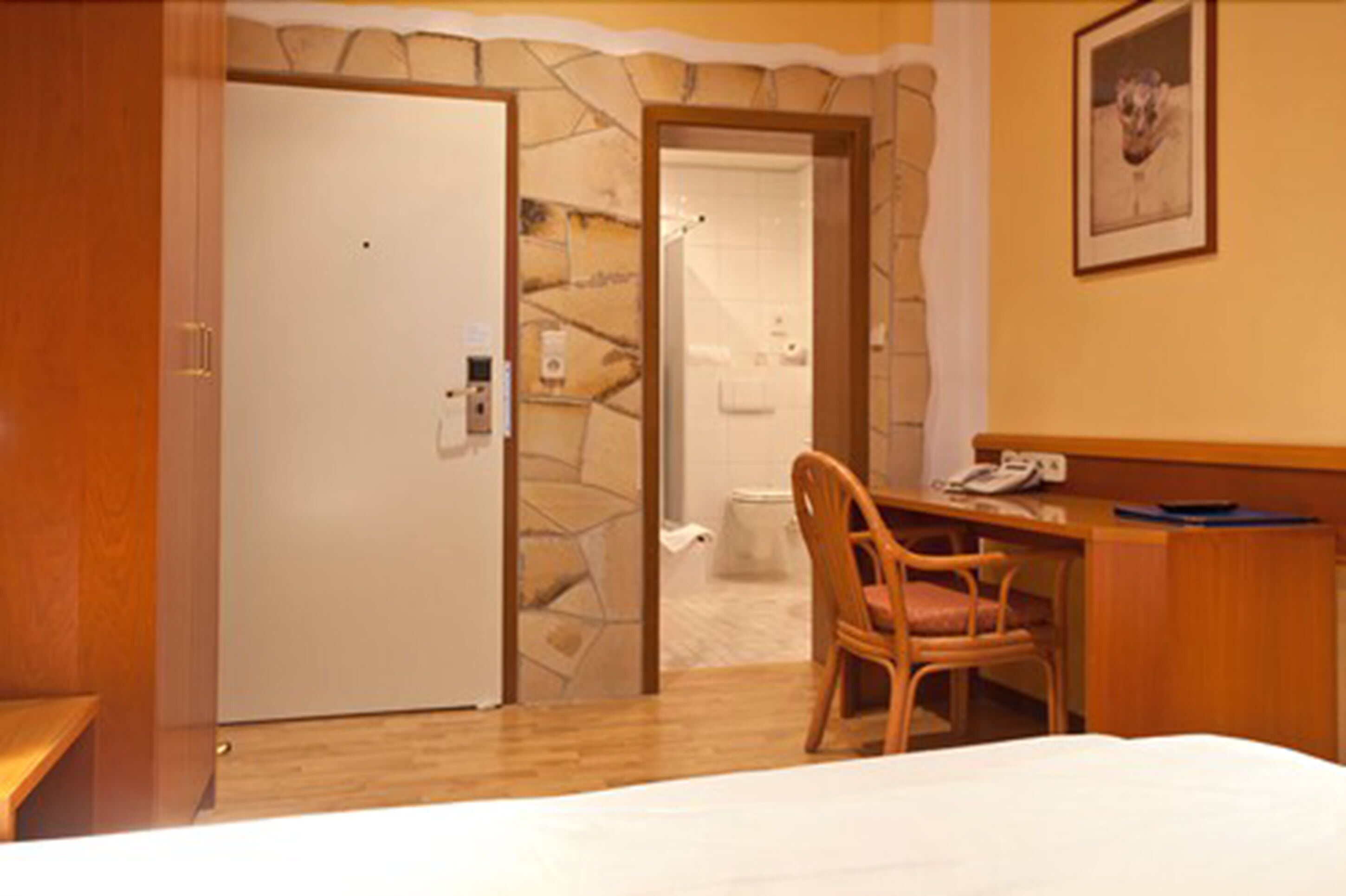 A hotel room with a bed, a desk with a chair, a telephone, and a bathroom visible through an open door.