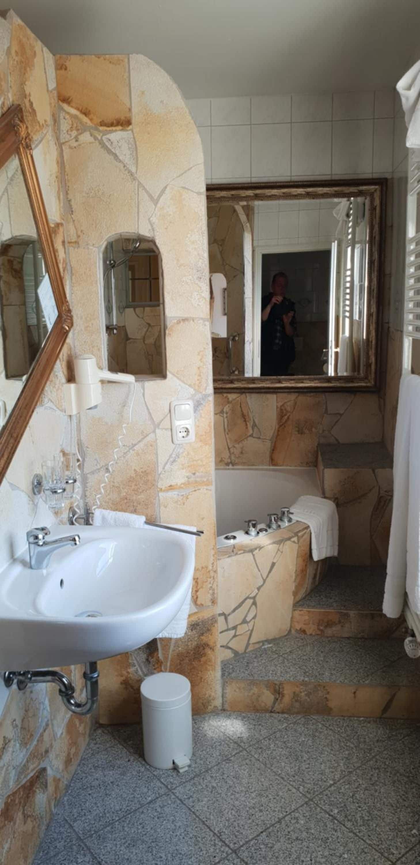 A bathroom with a stone wall, a sink, a mirror, a bathtub, and a shower.