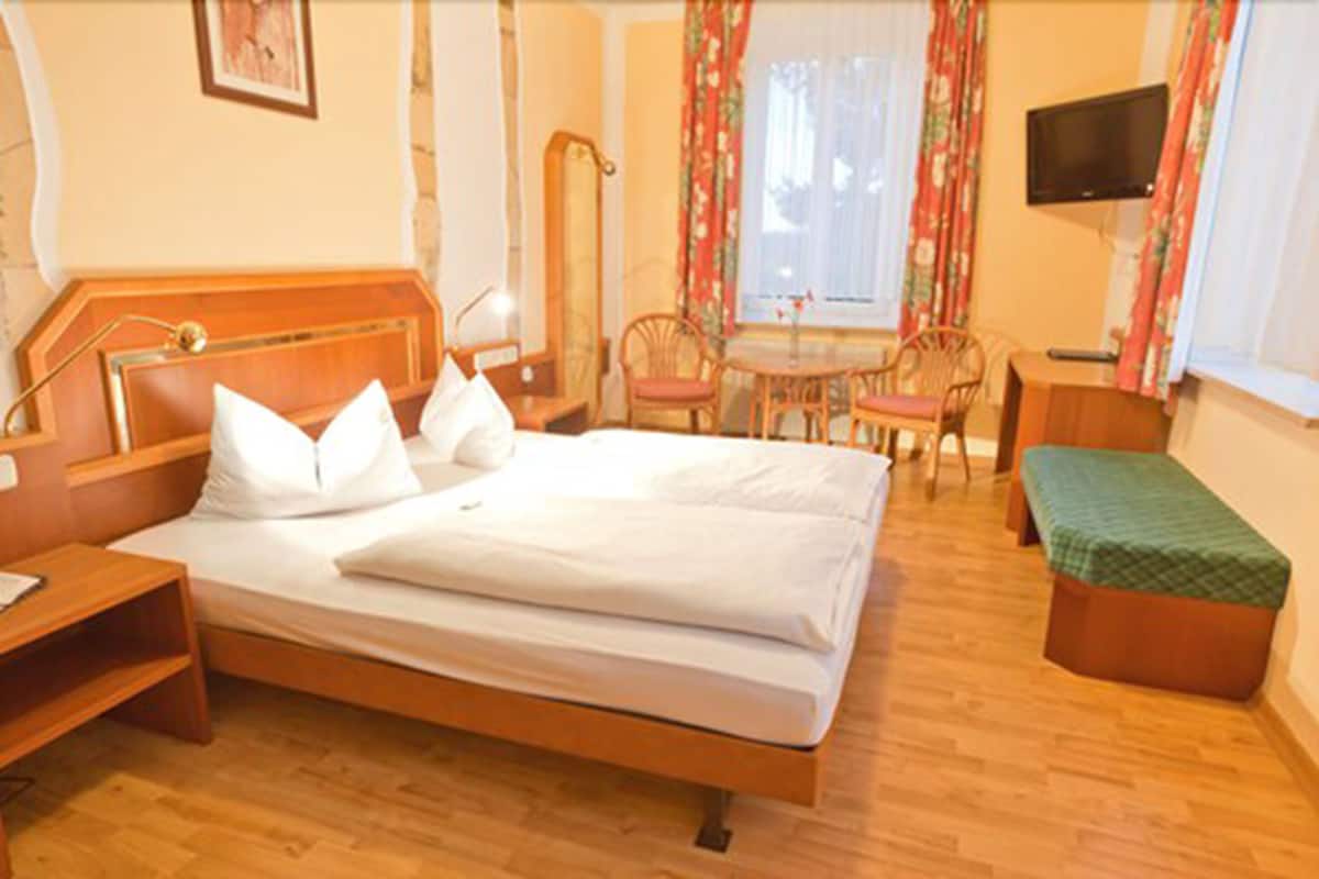 A hotel room with a wooden bed, a desk, a chair, a small table, and a TV.