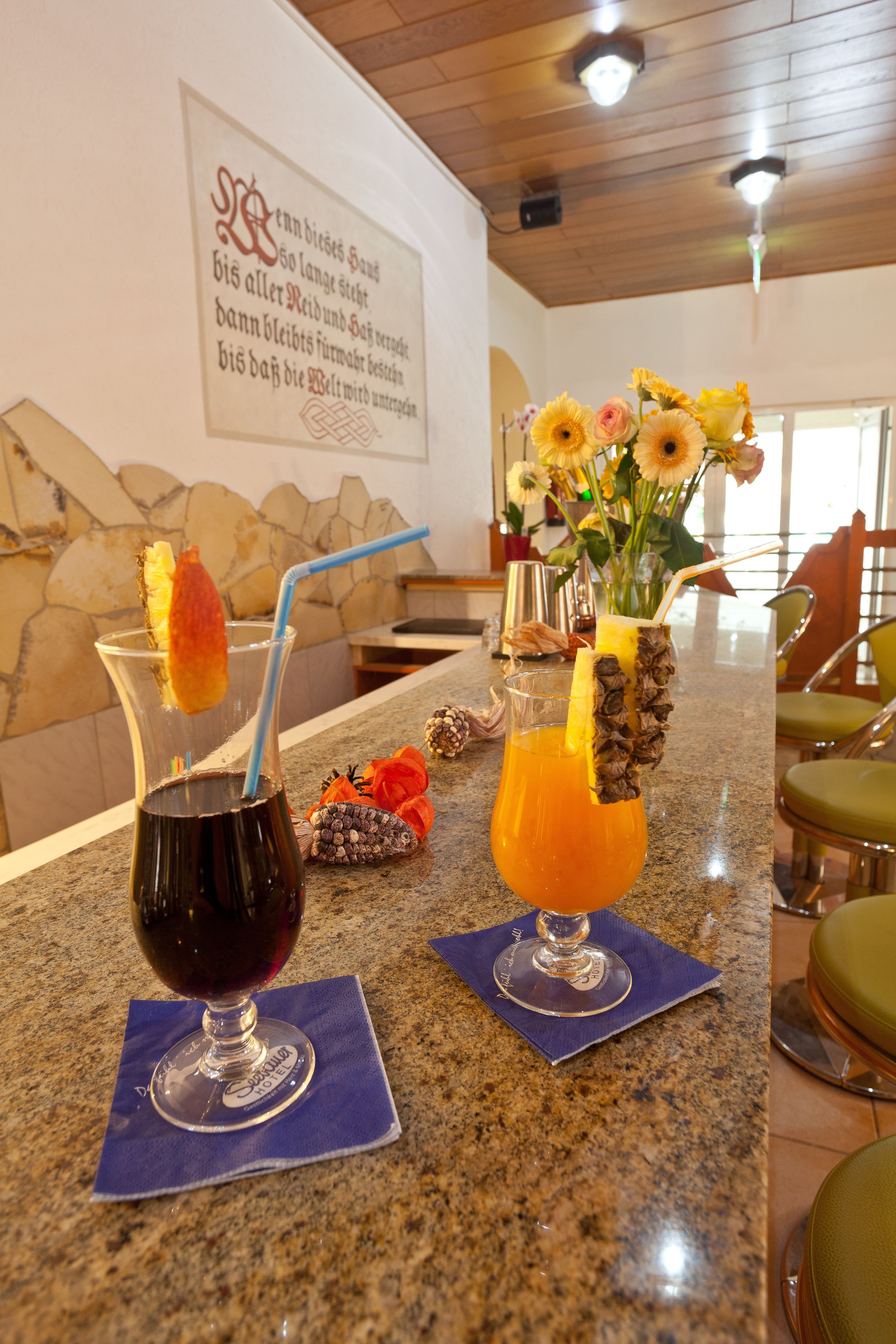 Two drinks on a bar counter with a stone wall and a wooden ceiling in the background.