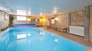 An indoor swimming pool with a tiled floor, stone walls, and a bench near the pool. - Seebauer Hotel Gut Wildbad (Wemding)