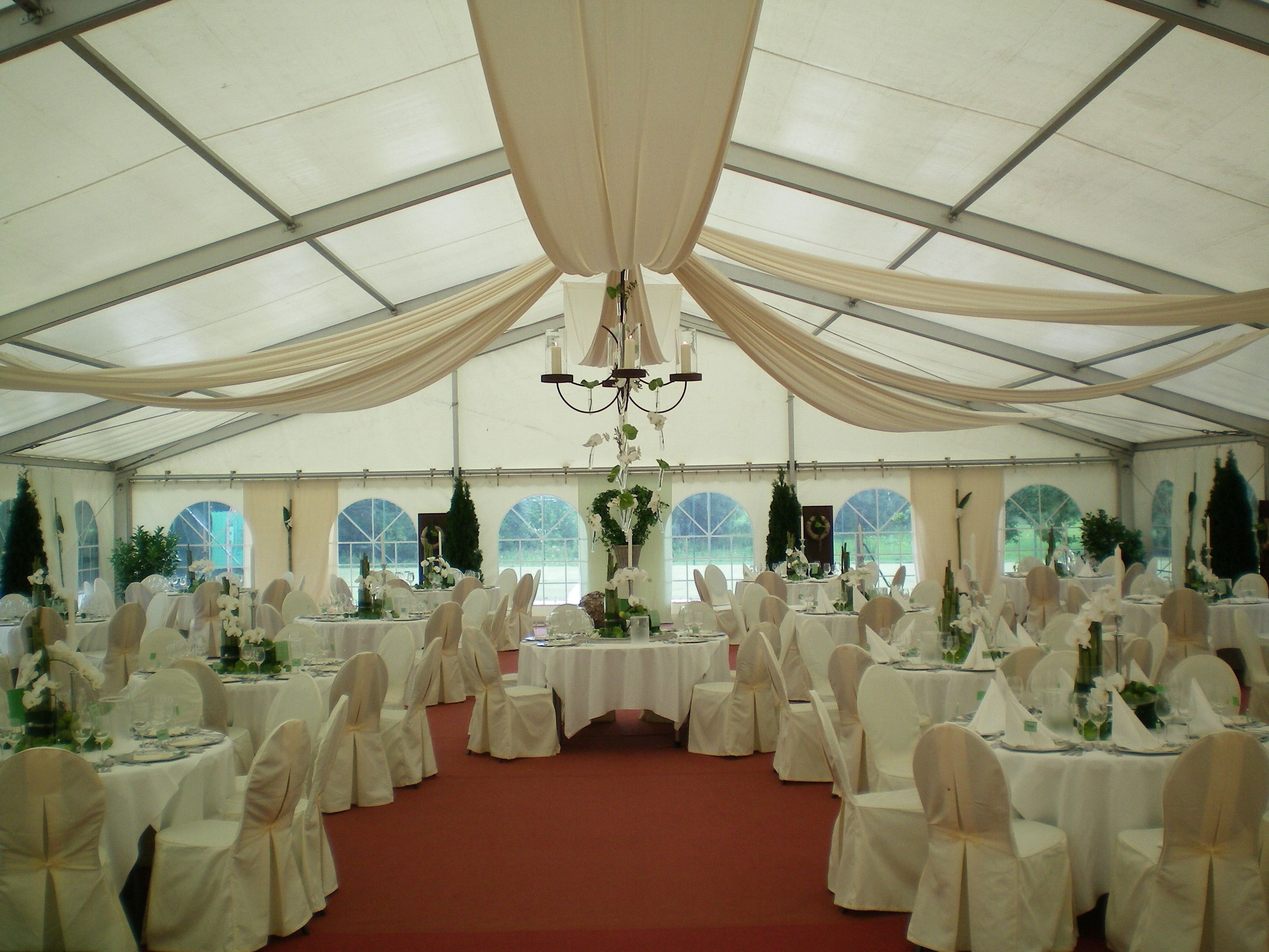 Un espacio para eventos con carpas, mesas redondas, manteles blancos y sillas con fundas blancas.