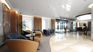 Un moderno vestíbulo de hotel con una zona de estar curvilínea, un mostrador de recepción y un separador de vidrio.