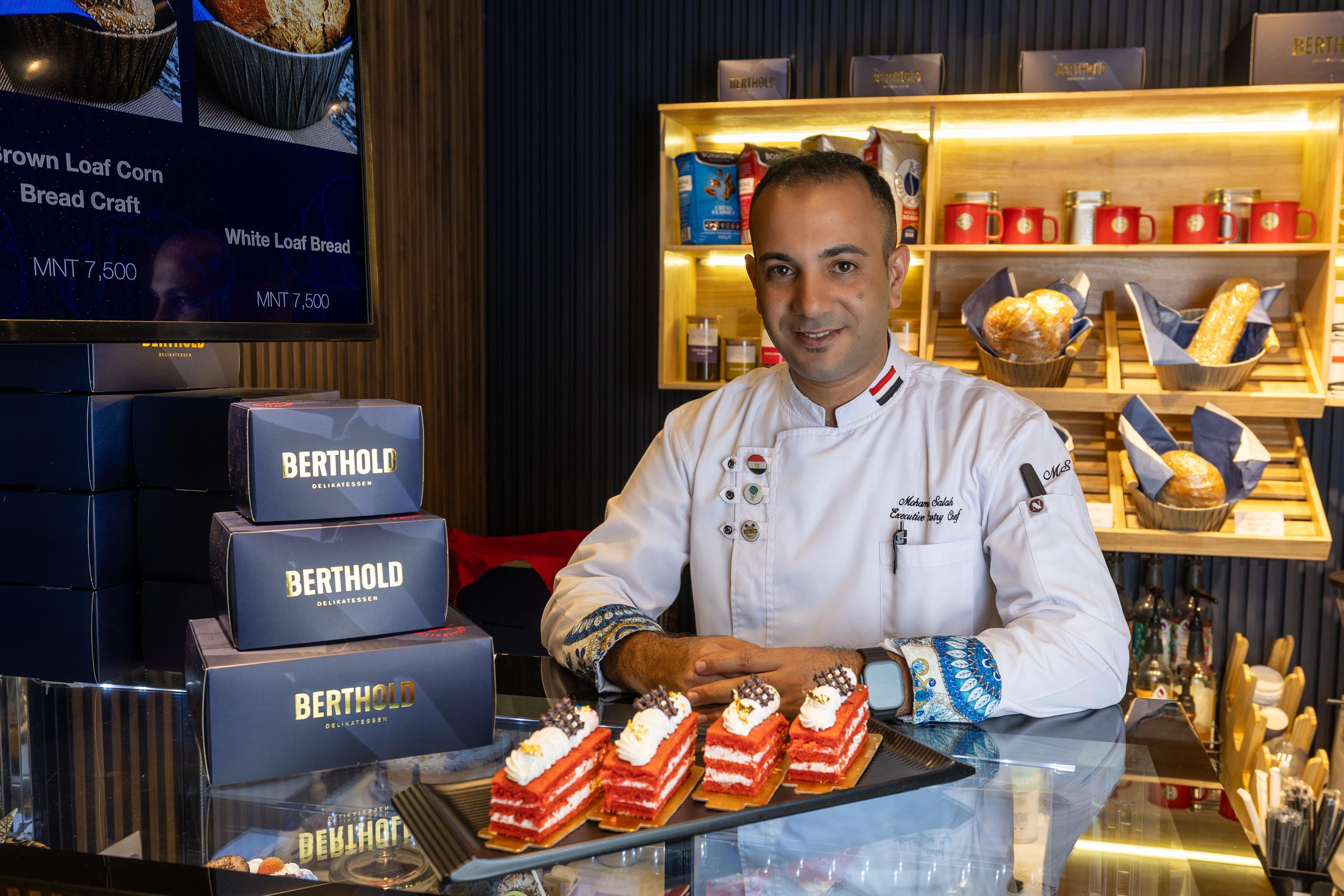 A chef presenting red velvet layered cake with whipped cream and chocolate decorations.