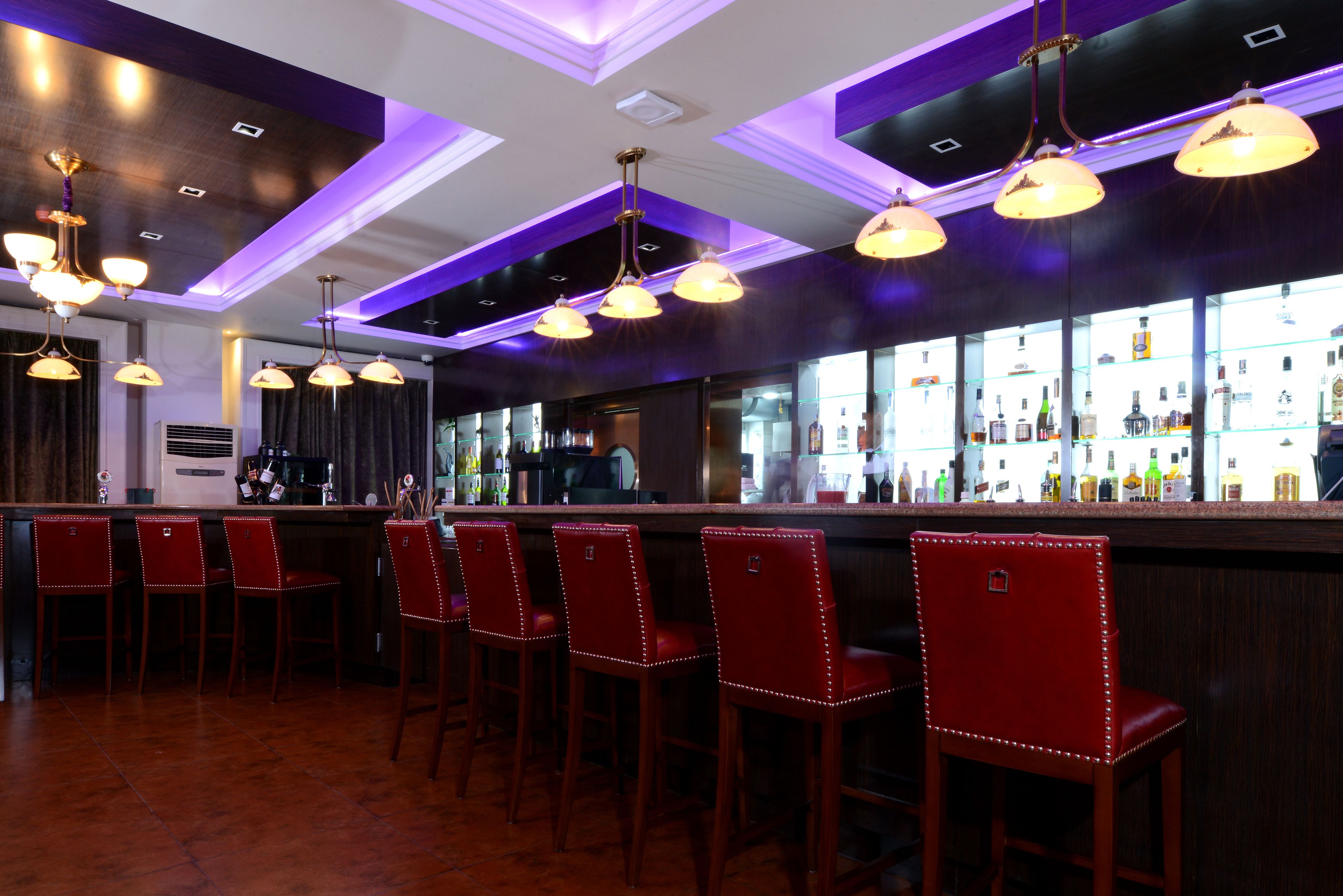 Zona de bar con taburetes rojos, mostrador con botellas e iluminación colgante.