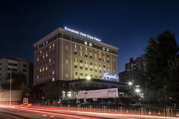 Un hotel de varios pisos con señalización iluminada, una entrada destacada y un entorno urbano circundante.