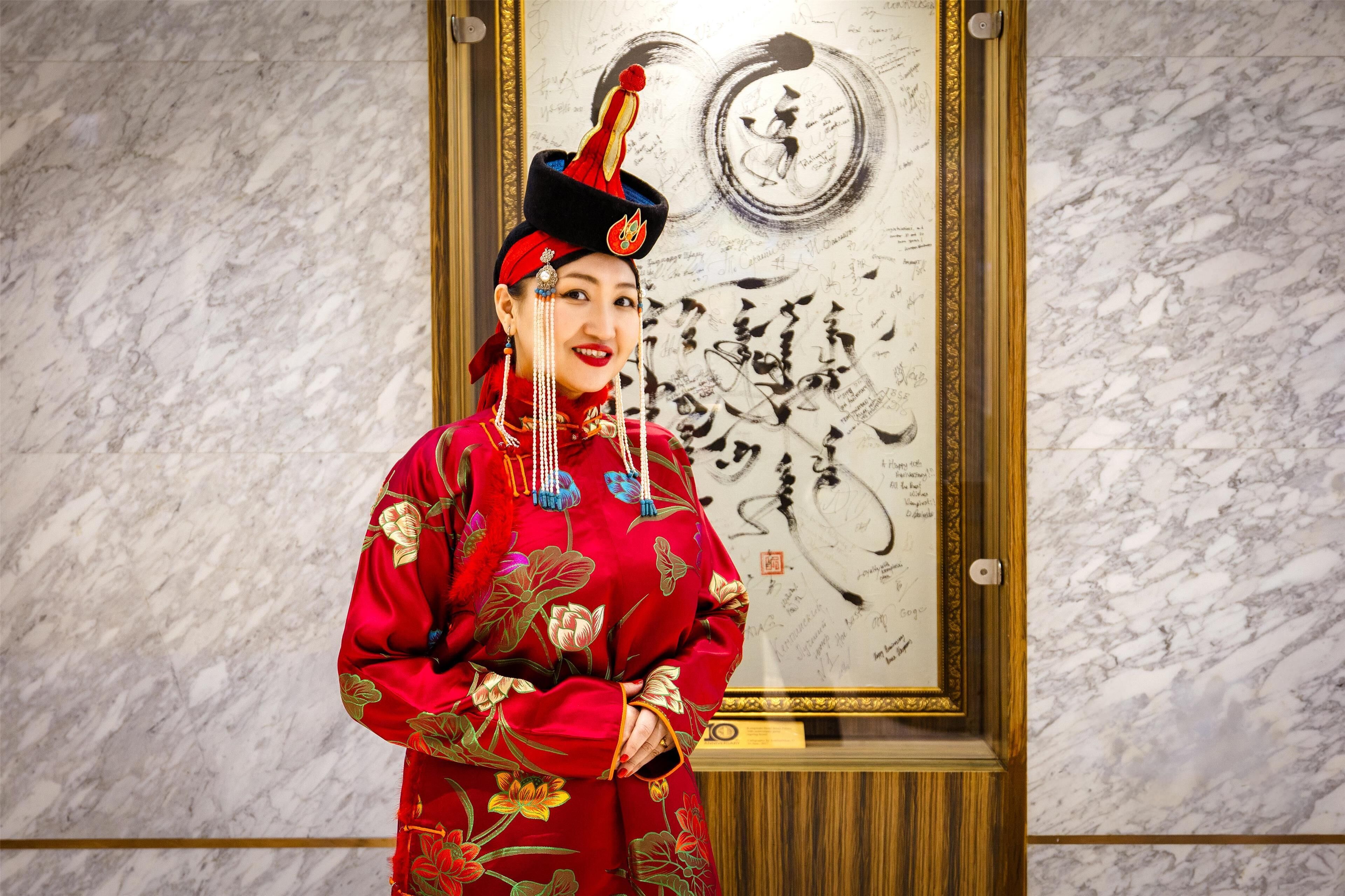 A person in traditional attire standing in front of a framed artwork on a marble wall.