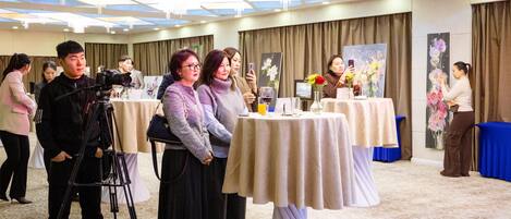 A room with tables set up for a meeting or event, a camera on a tripod, and people engaged in conversation.