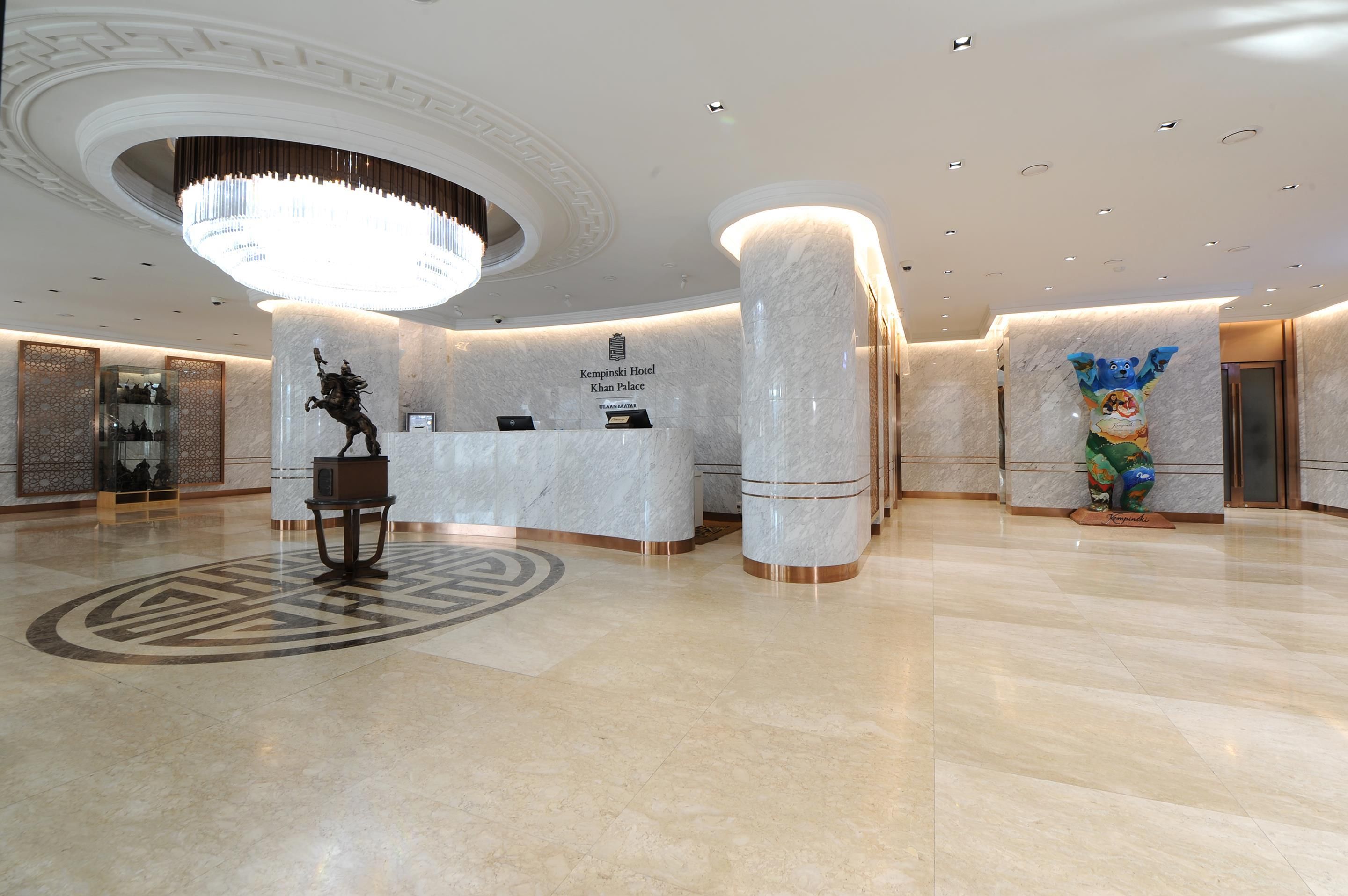 A hotel reception area with a marble floor, a large chandelier, and a statue of a horse.