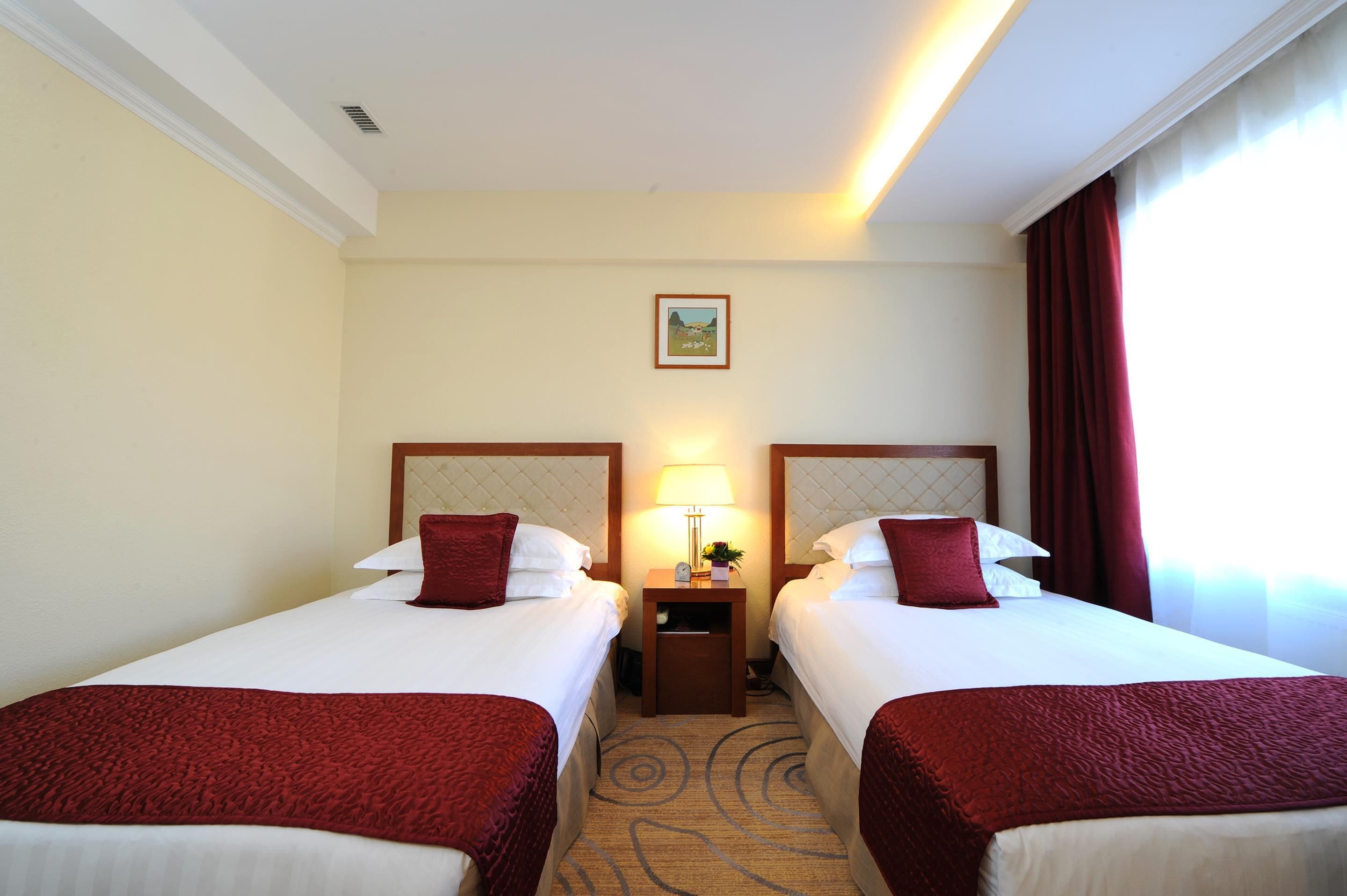 A hotel room with two beds, each with a headboard, a nightstand with a lamp, and a painting on the wall.