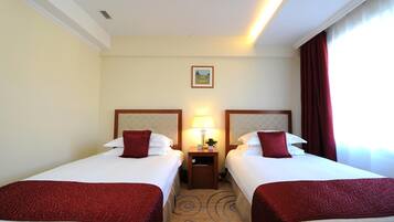 A hotel room with two beds, each with a headboard, a nightstand with a lamp, and a painting on the wall.