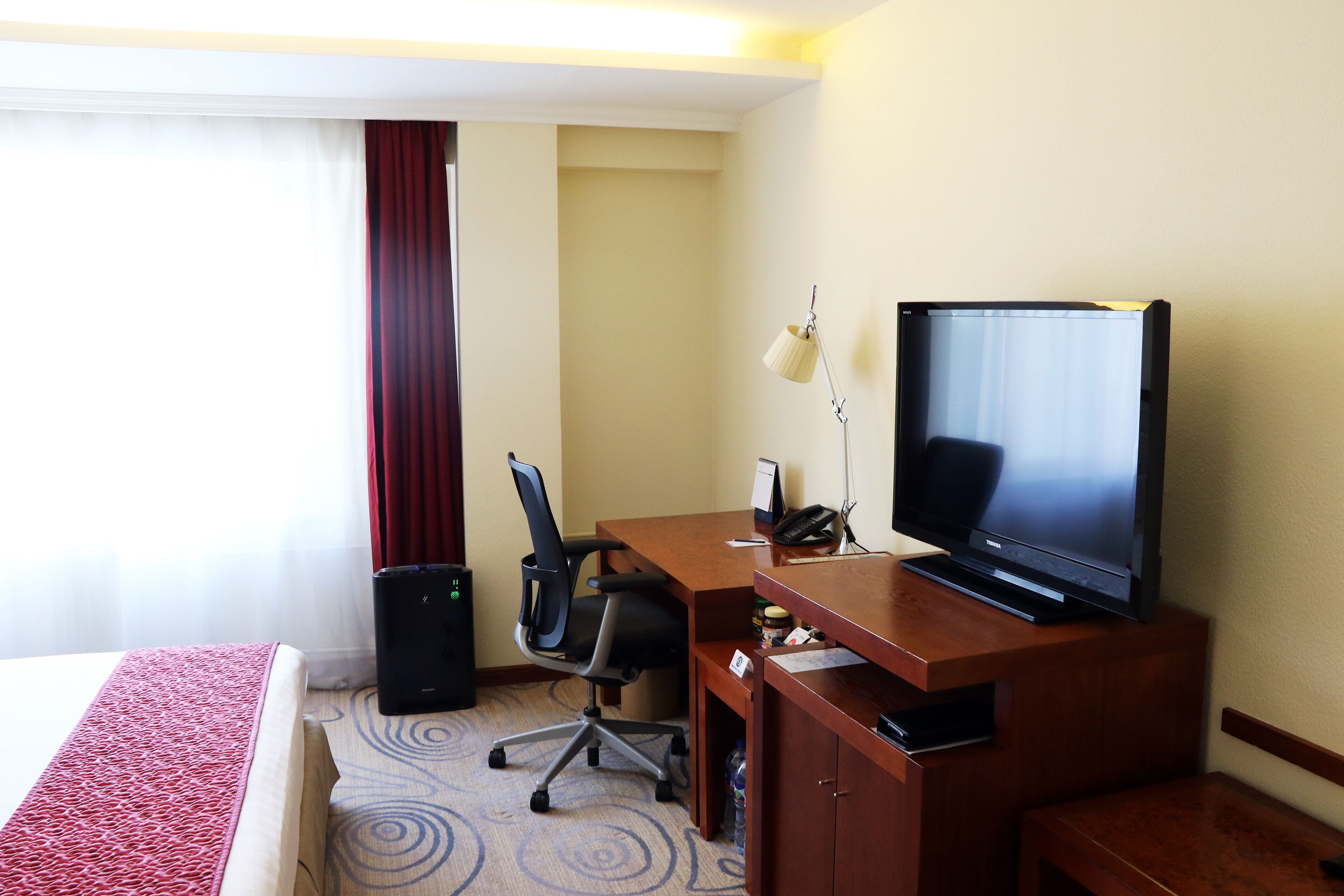 Una habitación de hotel con cama, escritorio con televisor, silla, lámpara y altavoz.