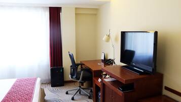 Una habitación de hotel con cama, escritorio con televisor, silla, lámpara y altavoz.