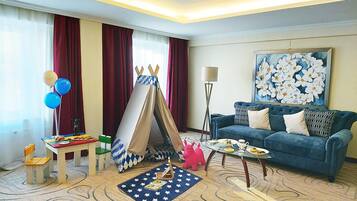 Una habitación de hotel con un sofá azul, un cuadro, un tipi, un tapete con estampado de estrellas y una pequeña mesa con comida y bebidas.