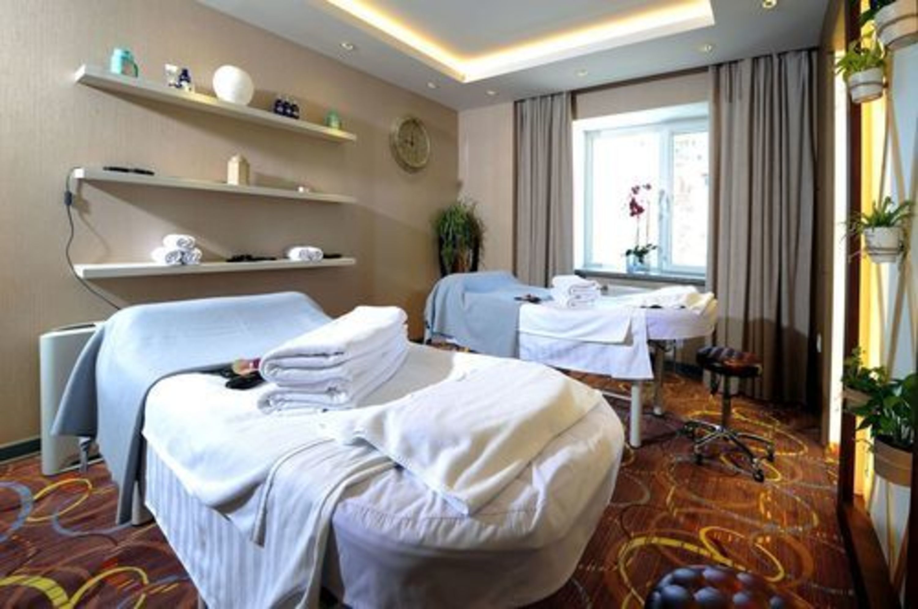 Habitación de hotel con dos camas, una ventana con cortinas, una planta y un estante en la pared con artículos de aseo.