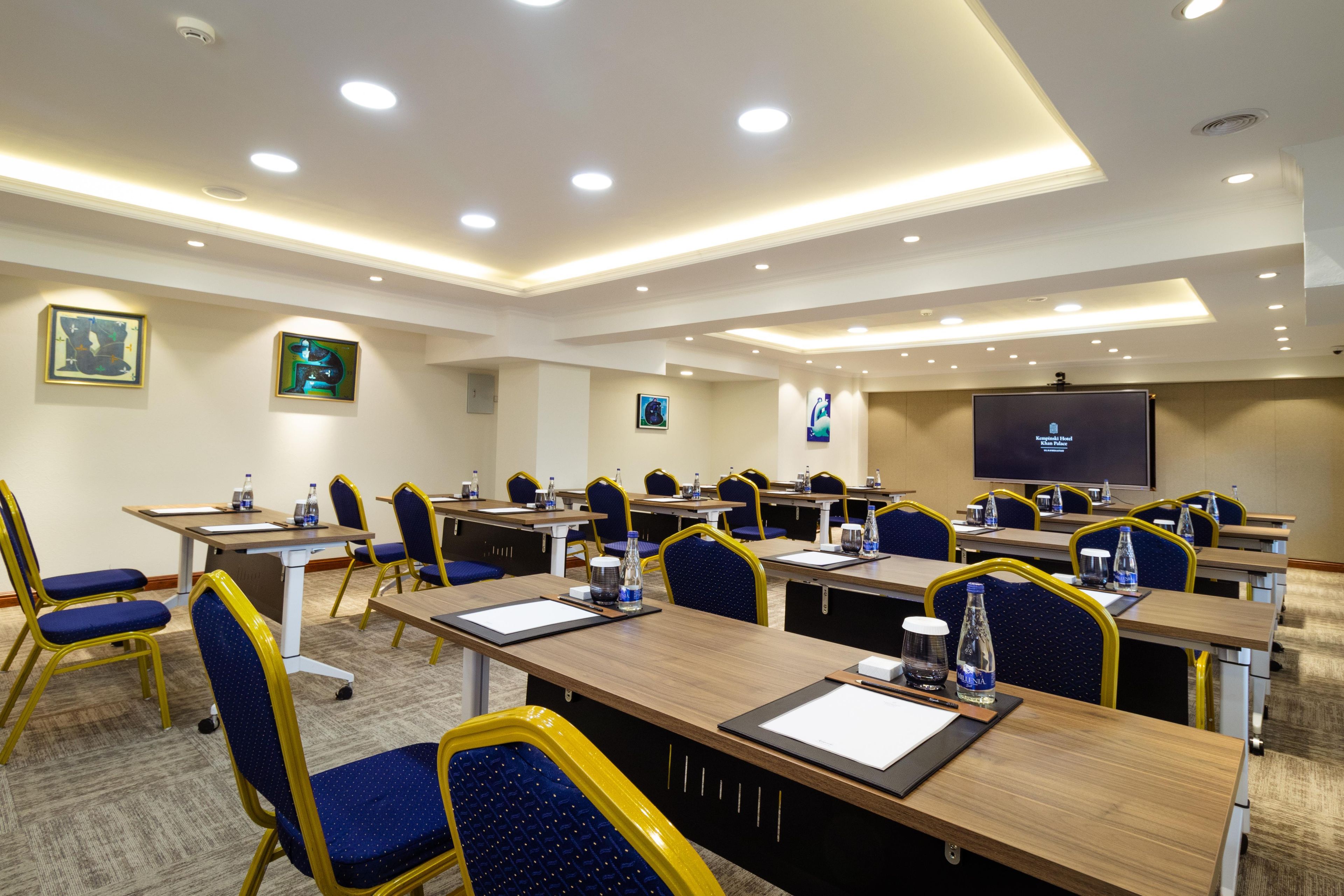 Un salón de conferencias con varias mesas y sillas, equipado con botellas de agua y blocs de notas.