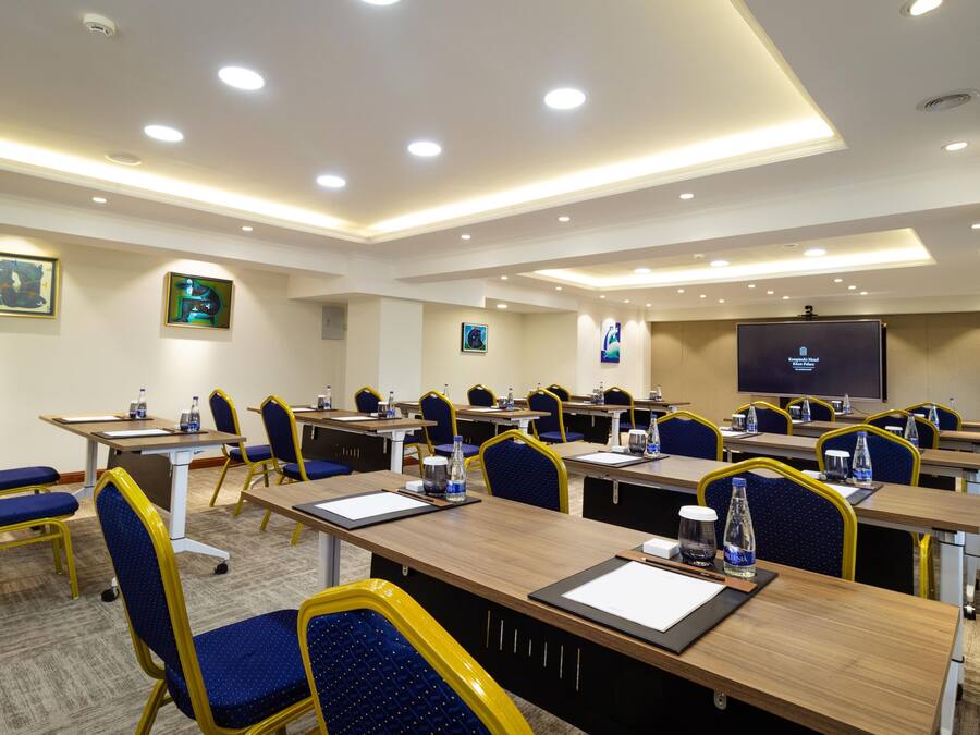 Un salón de conferencias con varias mesas y sillas, equipado con botellas de agua y blocs de notas.