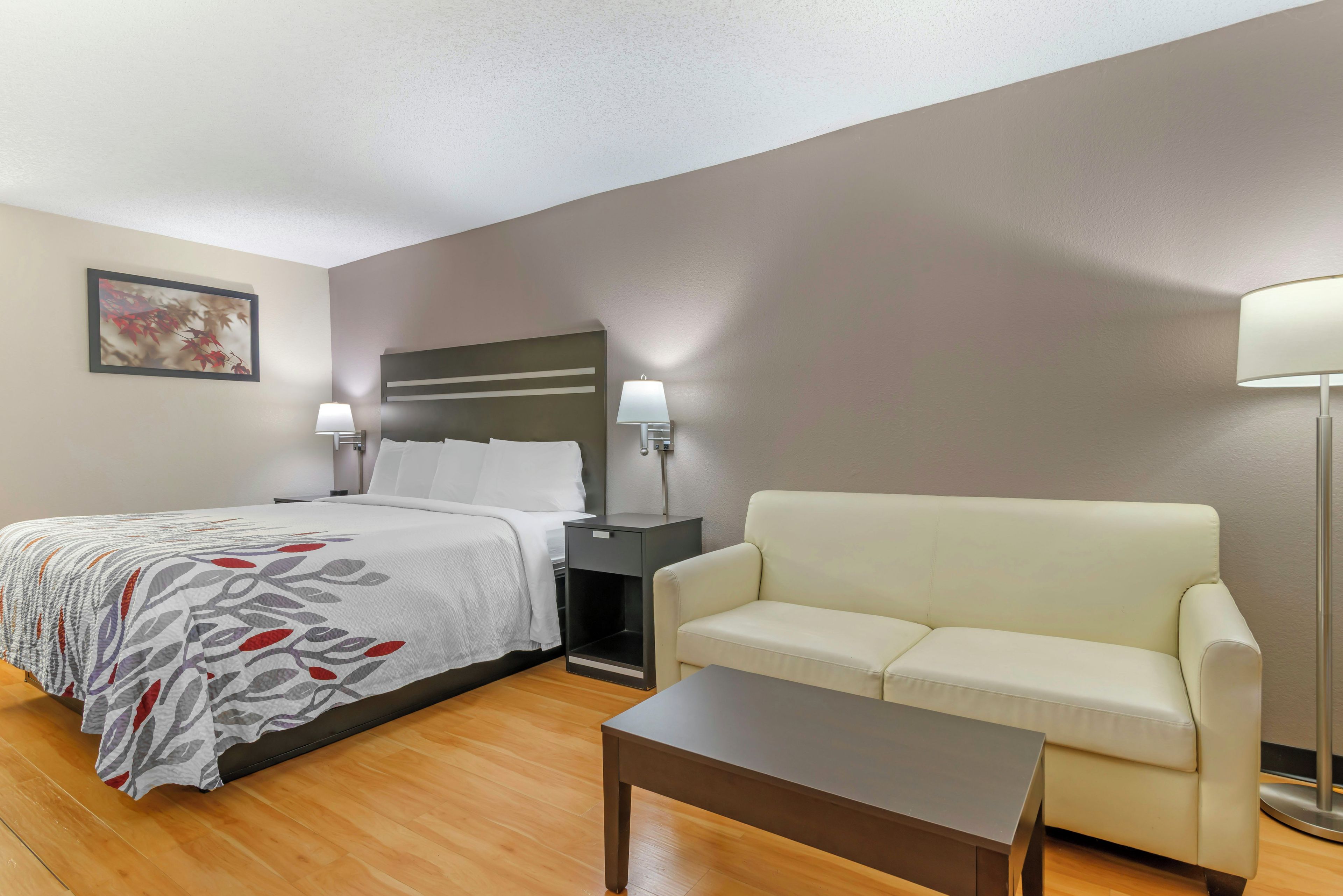 Una habitación de hotel con cama, sofá, mesita de noche, lámpara y mesa de centro.