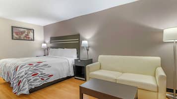 Una habitación de hotel con cama, sofá, mesita de noche, lámpara y mesa de centro.