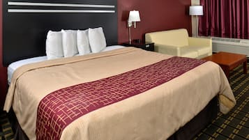 Een hotelkamer met een groot bed, een nachtkastje, een lamp, een stoel en een raam met gordijnen.
