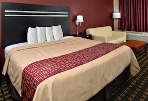 Ein Hotelzimmer mit einem großen Bett, einem Nachttisch, einer Lampe, einem Sessel und einem fenster mit Vorhängen.
