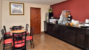 Un coin repas avec une table en bois et des chaises rouges, un comptoir de cuisine avec divers appareils et des produits alimentaires, et un tableau encadré accroché au mur.