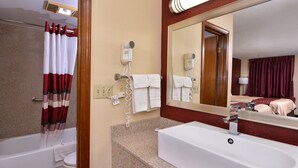 A hotel bathroom with a bathtub, a sink, a mirror, and a hairdryer on the wall.