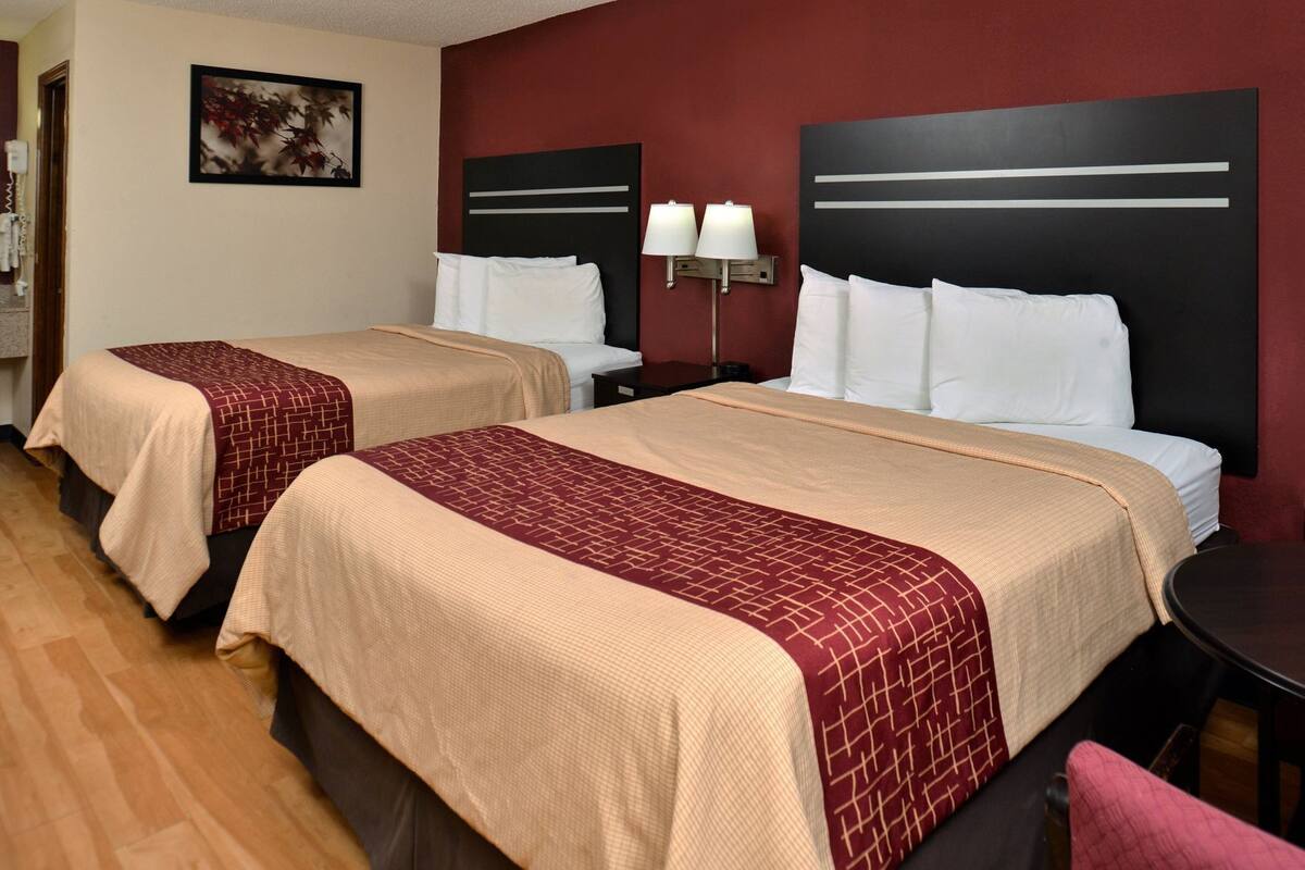 A hotel room with two beds, a nightstand with lamps, a framed picture on the wall, and a wooden floor.