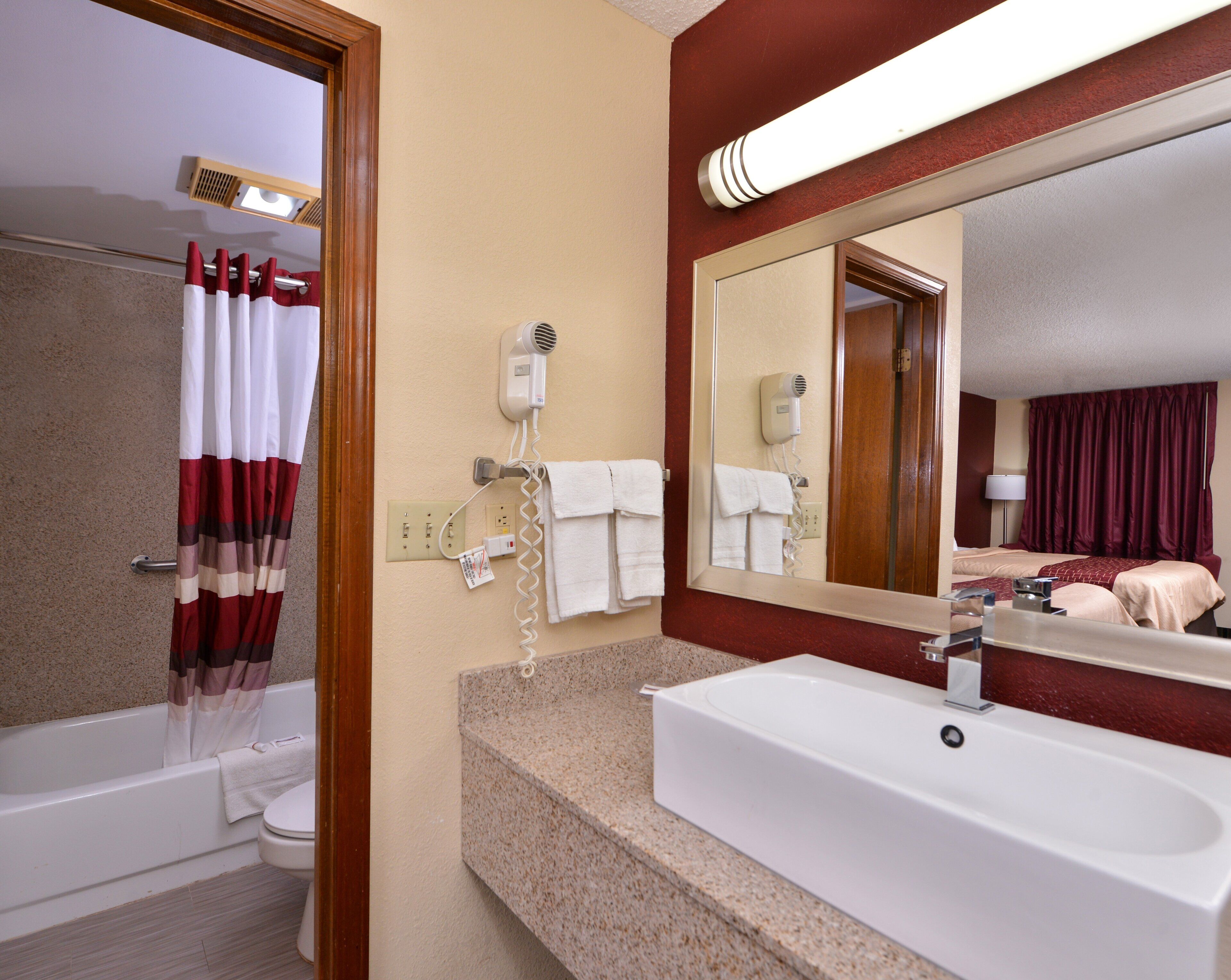 A hotel bathroom with a bathtub, a sink, a hairdryer, and a mirror.