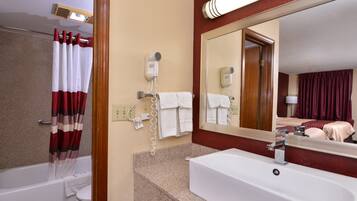 A hotel bathroom with a bathtub, a sink, a hairdryer, and a mirror.