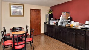 A dining area with a wooden table and red chairs, a kitchen counter with appliances, and a door.