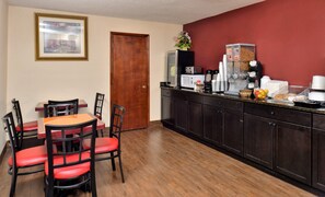 Un comedor con mesa de madera y sillas rojas, una encimera de cocina con electrodomésticos, y una puerta.