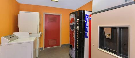 A hallway with a vending machine, a door, and a refrigerator.
